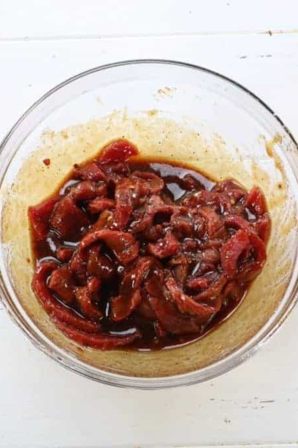 Sliced beef strips submerged in dark soy-teriyaki marinade in a covered bowl, prepped for air fryer beef jerky