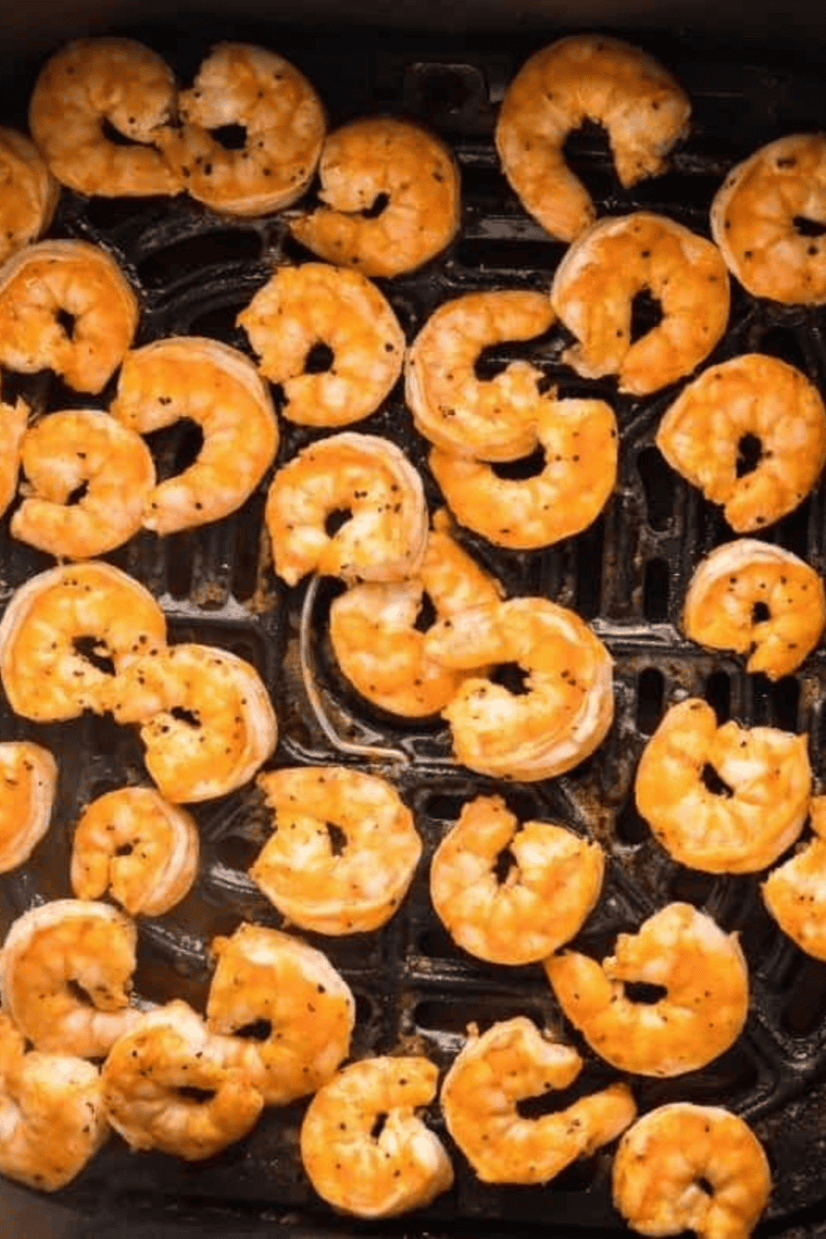 Raw shrimp coated in olive oil arranged in an air fryer basket ready to cook.