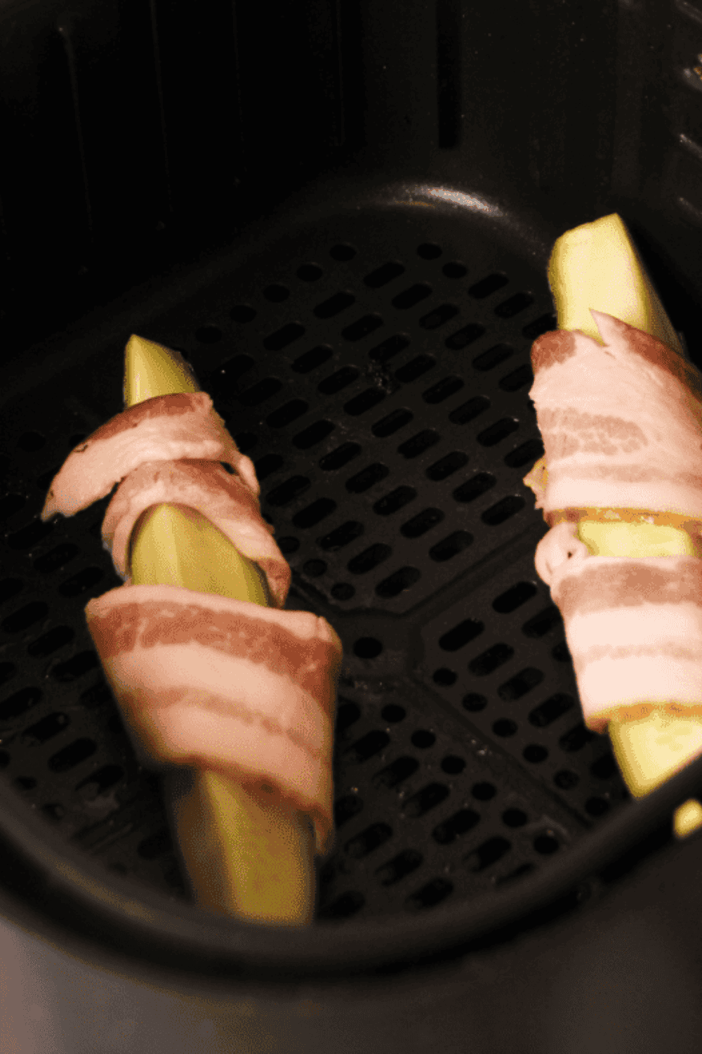 Bacon-wrapped zucchini cooking in an air fryer until golden and crispy.