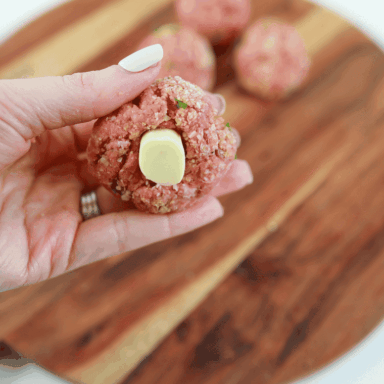Pressing a mozzarella cube into the center of each meatball.