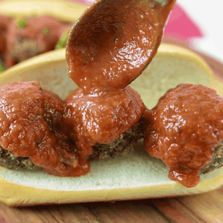 Homemade Maggiano’s-style meatballs in rich marinara sauce served on a plate with garnish.