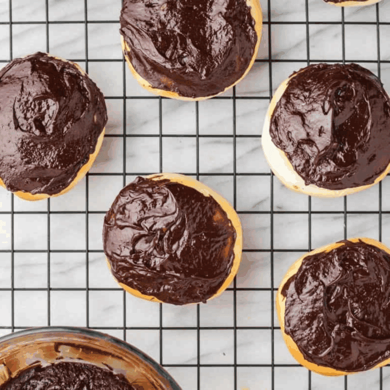 Spreading melted chocolate over the tops of Bavarian cream donuts