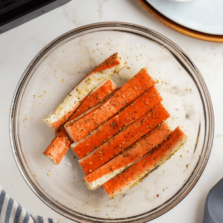Imitation crab pieces tossed with melted butter and Old Bay seasoning in a mixing bowl.