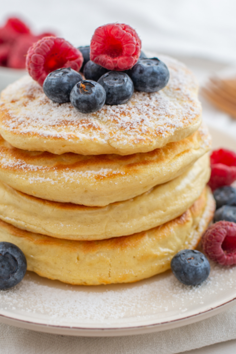 Stack of reheated fluffy pancakes with butter and syrup on white plate