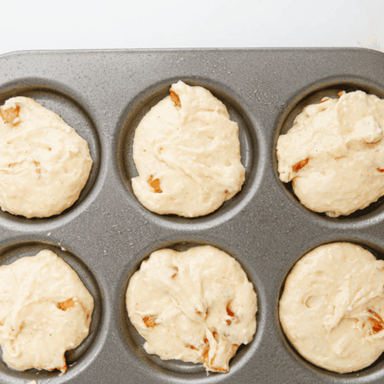 Gently folding coated apple pieces into muffin batter without crushing