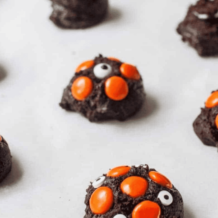 Dark chocolate cookie dough balls topped with orange M&M's and white candy eyeballs arranged in a black air fryer basket before cooking.