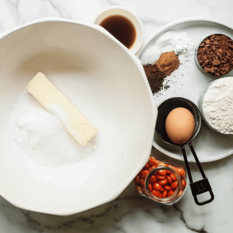 A close-up of a stand mixer bowl containing pale, creamed butter and sugar being blended with a fresh egg and vanilla extract for a smooth cookie dough base.