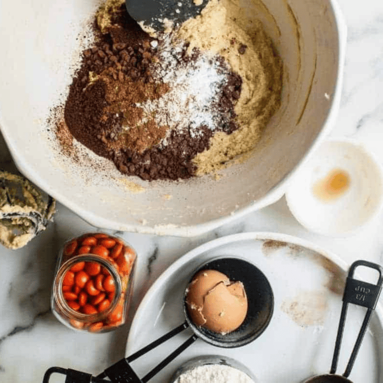 Dark cocoa powder and dry dry coffee being gently folded into a creamed butter and sugar mixture with a rubber spatula in a metal mixing bowl.