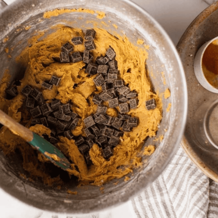 Pumpkin cookie dough with spices and chocolate chips being mixed.