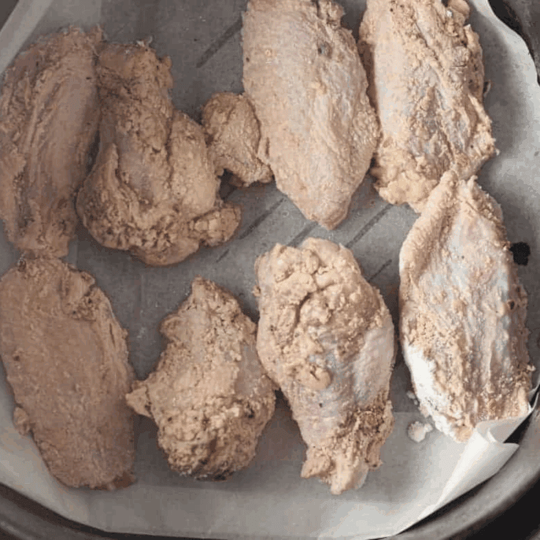 Wings arranged in a single layer in the air fryer basket for even cooking.