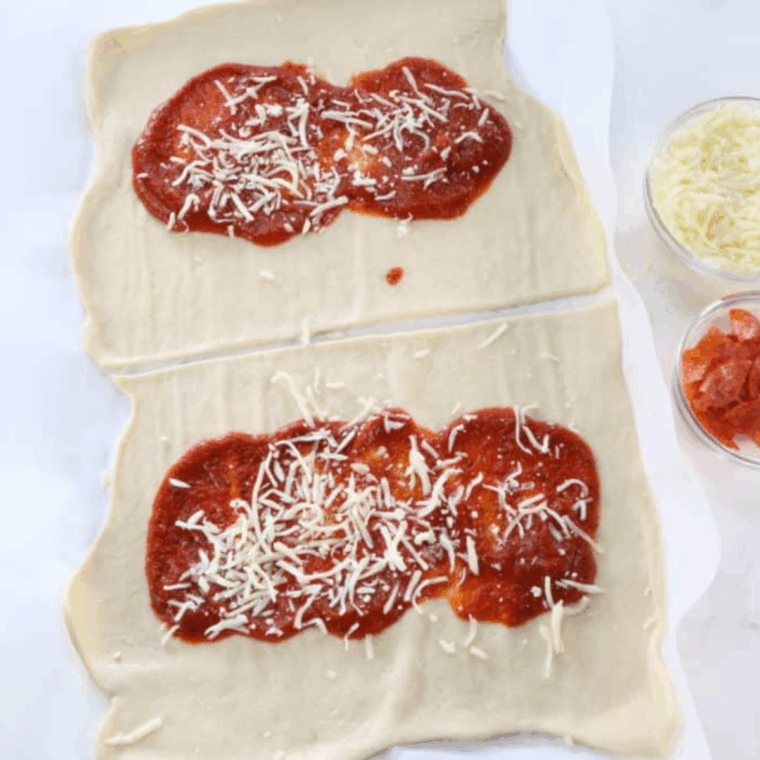 Pizza dough with pizza sauce spread in the center and shredded mozzarella sprinkled on top.