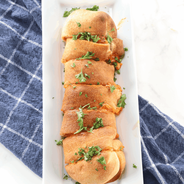 Rolled stromboli in air fryer basket, sprayed with oil and seasoned with garlic and onion powder.