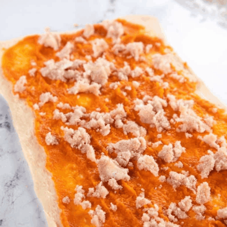 crescent dough pressed into a rectangle topped with pumpkin puree and sprinkled sugar spice mixture