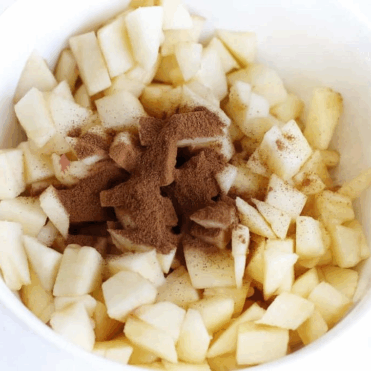 Chopped apple pieces mixed with cinnamon, brown sugar, and melted butter in a bowl, coated evenly.