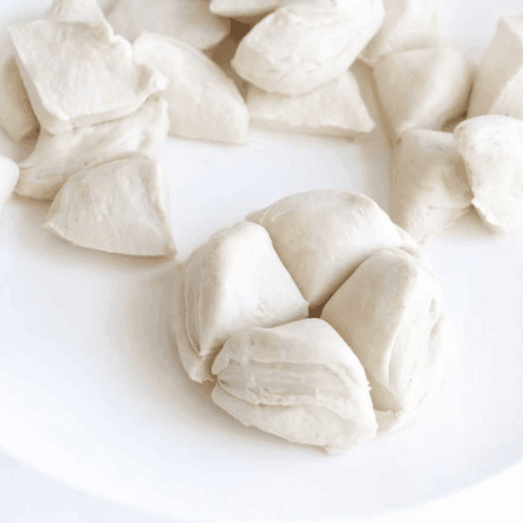 Biscuit dough cut into quarter pieces and placed in a large mixing bowl.
