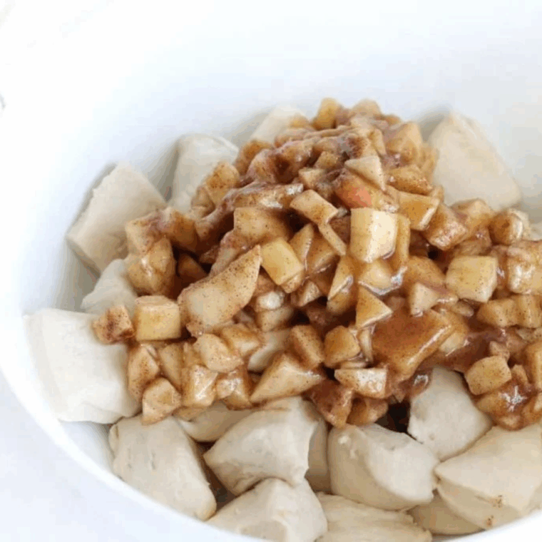 Biscuit pieces in a bowl being coated evenly with apple, cinnamon, brown sugar, and butter mixture.