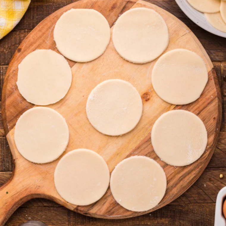 Circles cut from stacked refrigerated pie crust with a biscuit cutter on a wooden board