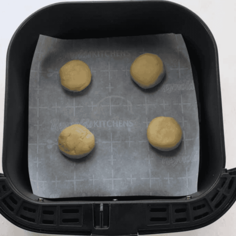 Lofthouse cookie dough arranged on parchment paper in air fryer basket, ready to cook.