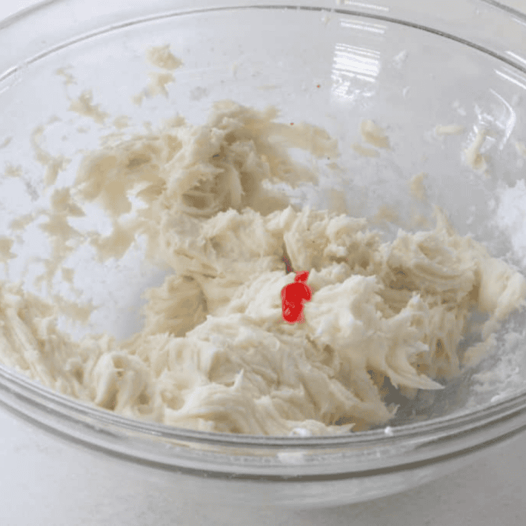 Mixing icing in a bowl with a few drops of pink food coloring.