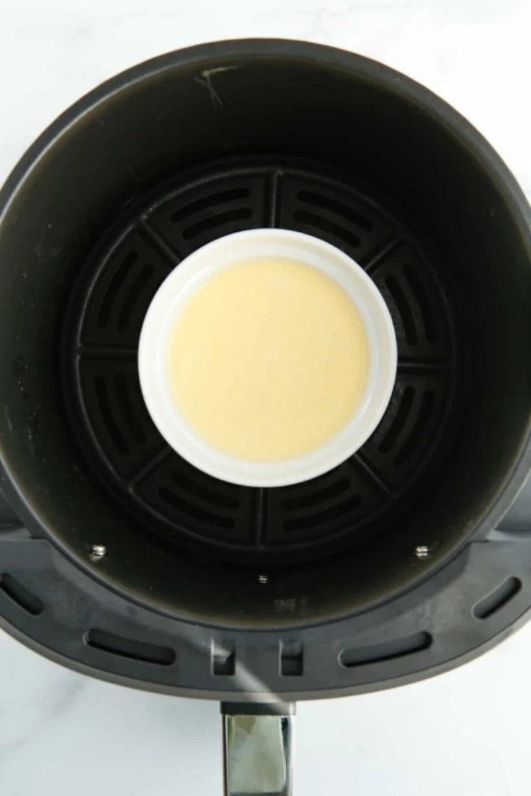 Four white ramekins filled with custard inside an air fryer basket