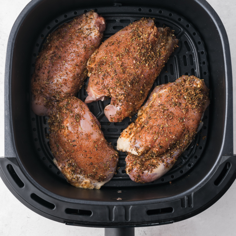 Marinated jerk chicken thighs in a single layer in an air fryer basket