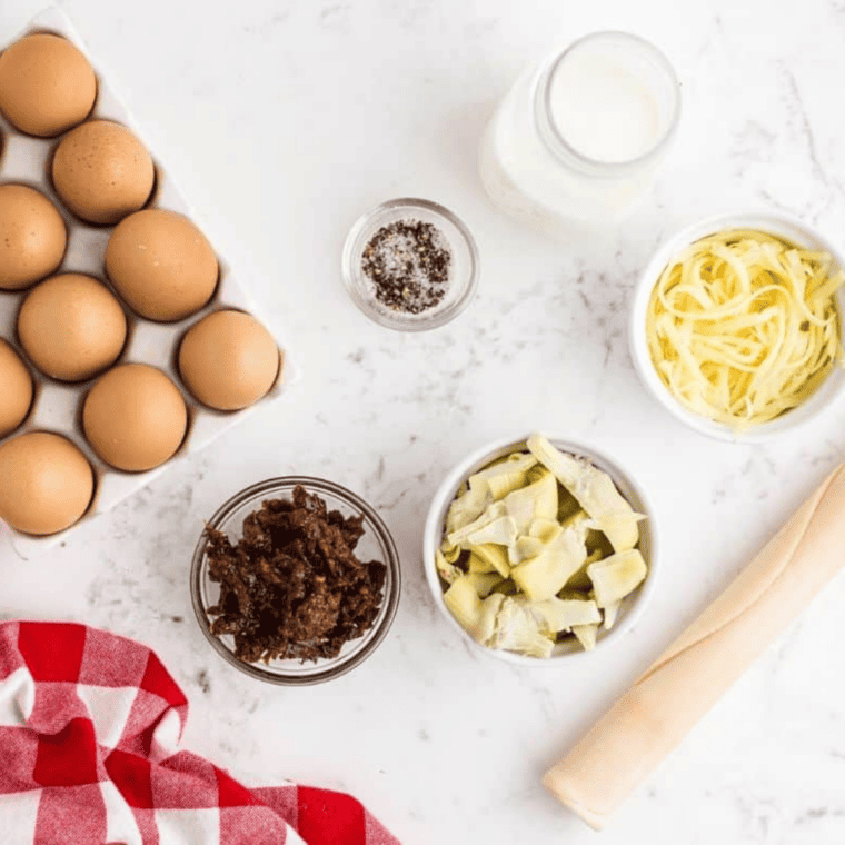 Ingredients for air fryer quiche: pie crust, jack cheese, artichoke hearts, sun-dried tomatoes, egg, and cream.