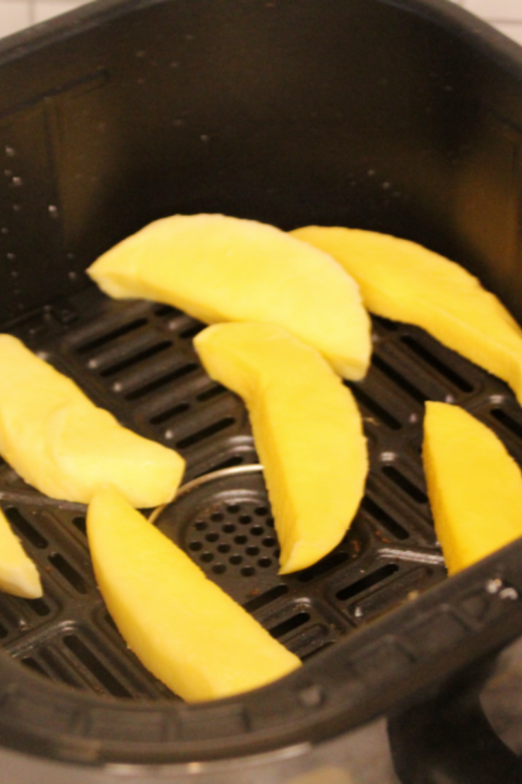 Mango slices arranged in a single layer in an air fryer tray, spaced apart to ensure even dehydration and proper airflow.
