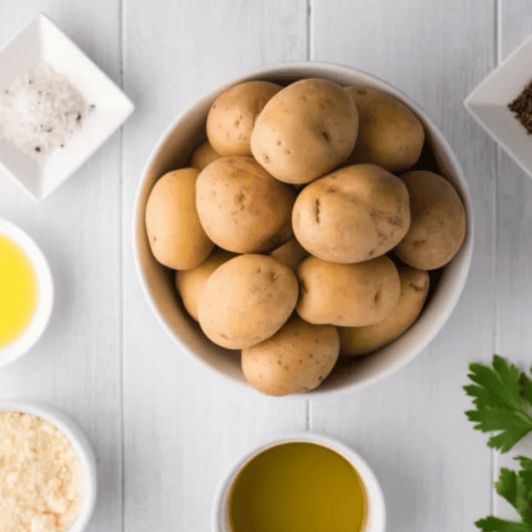 Ingredients for Crispy Air Fryer Greek Lemon Potatoes on a white table: potatoes, olive oil, lemon, garlic, and seasonings.