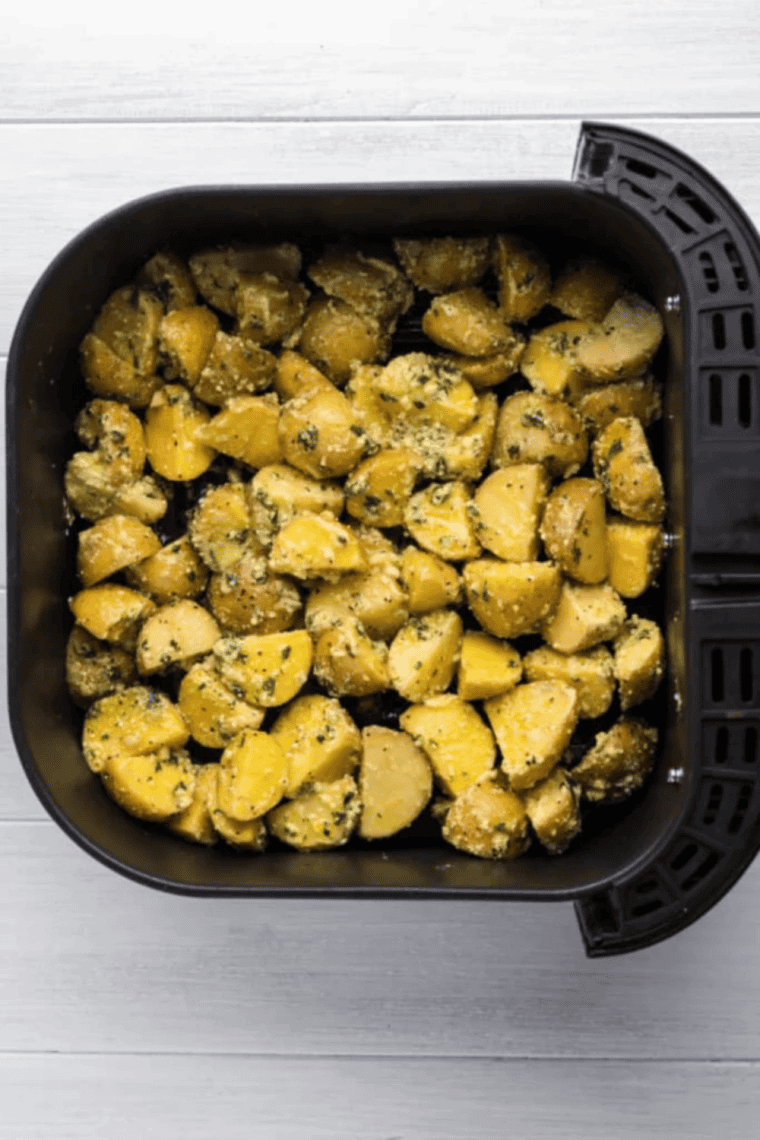 Seasoned potatoes in the air fryer basket, ready to cook for Crispy Air Fryer Greek Lemon Potatoes.
