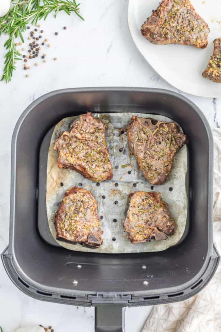 Seasoned frozen lamb chops arranged in a single layer in the air fryer basket before cooking