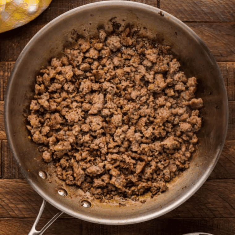 Ground beef, sausage, and diced onions browning in a preheated skillet, ready to be drained and cooked further.
