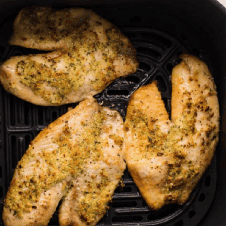 Golden and flaky Easy Air Fryer Frozen Tilapia fillets served with lemon wedges and fresh herbs on a plate.