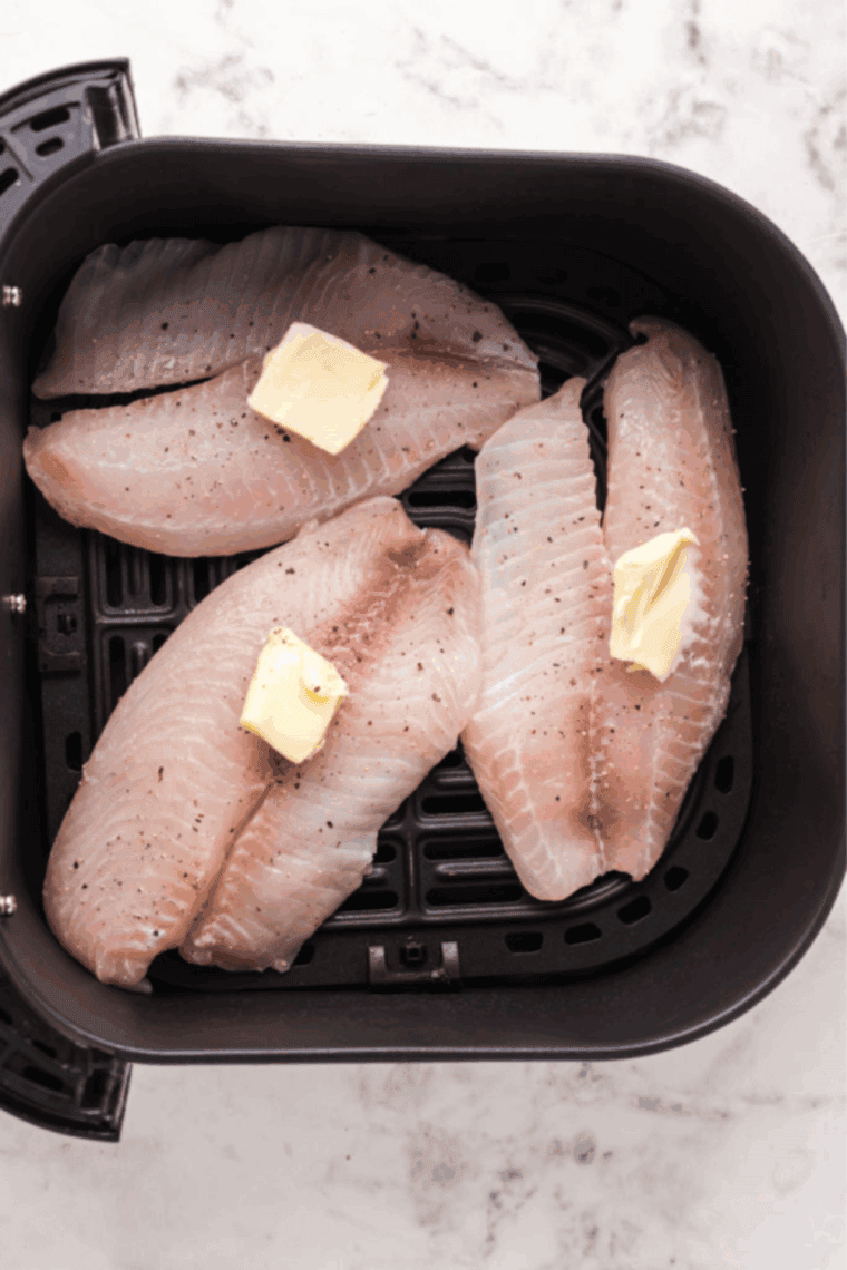 Seasoned frozen tilapia fillets arranged in a single layer in the air fryer basket, not overlapping.