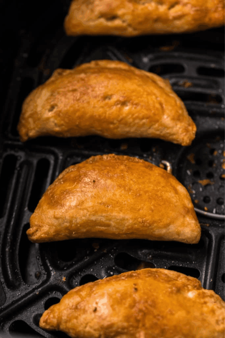 Air fryer basket filled with crispy golden meat pies.