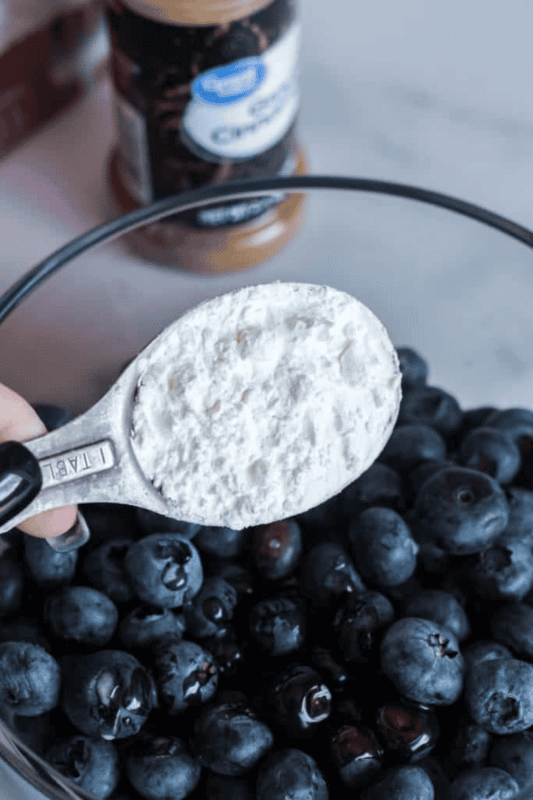 Blueberries mixed with melted butter, cinnamon, cornstarch, and sugar in a bowl, then topped with cake mix in a pan for Instant Pot blueberry cake preparation.