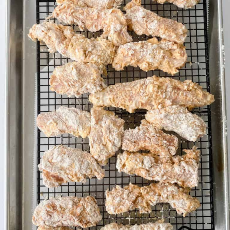 Chicken pieces arranged in an air fryer basket with space between them, ready to cook in batches for even crisping.