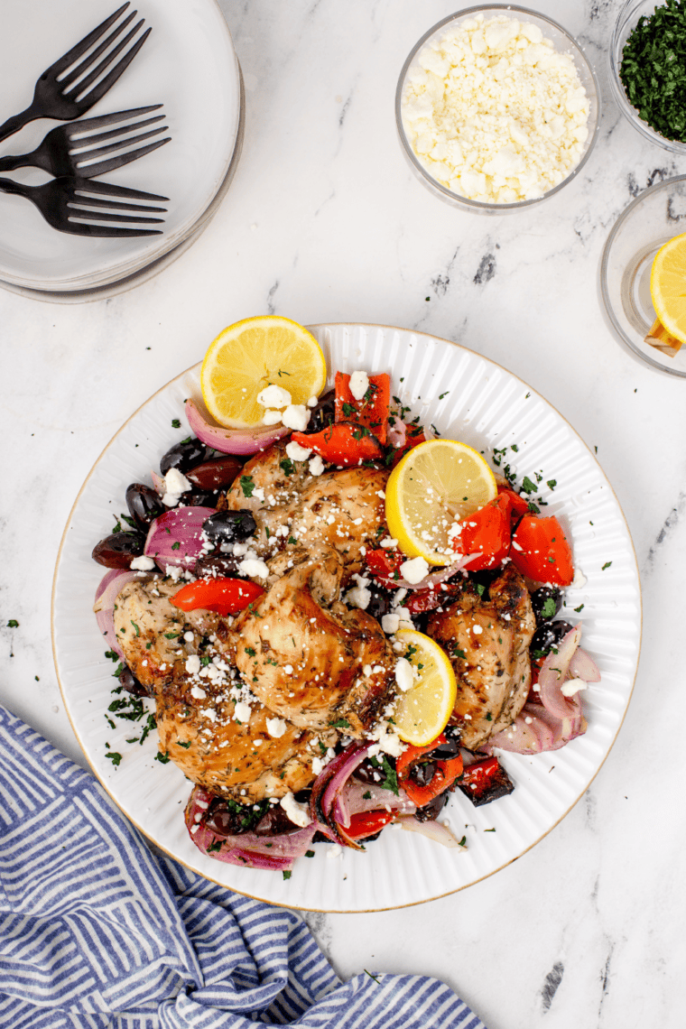 Close-up of air fryer Greek chicken thighs with red peppers, onion, and kalamata olives, garnished with feta and parsley
