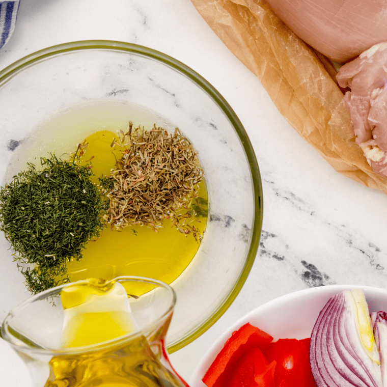 Olive oil, lemon juice, thyme, and dill whisked together in a bowl to make Greek chicken marinade
