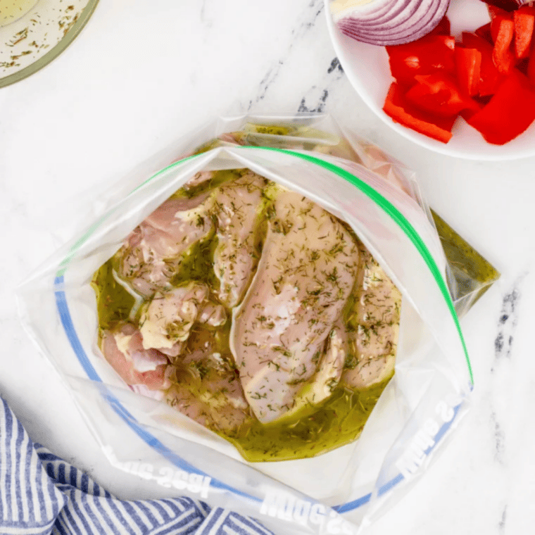 Chicken thighs, red pepper, red onion, and kalamata olives marinating in a resealable bag