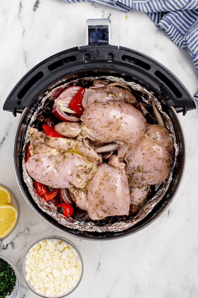 Marinated vegetables and chicken thighs arranged on foil in the air fryer basket, chicken on top