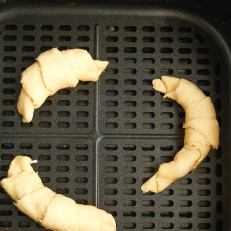 Unbaked peanut butter chocolate crescent rolls spaced apart in a greased air fryer basket