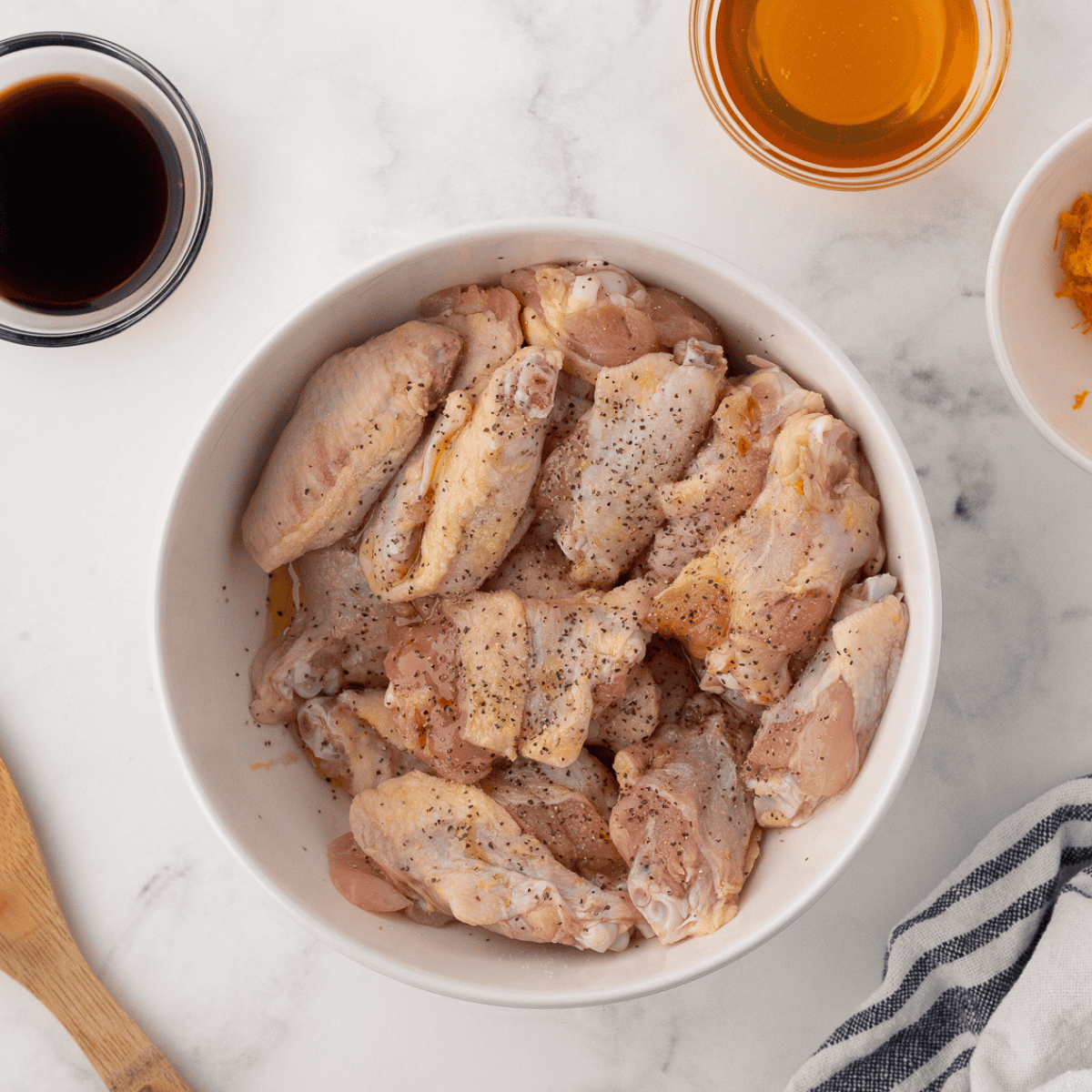 Raw chicken wings tossed with baking powder and salt in a glass bowl for crispy lemon pepper wings