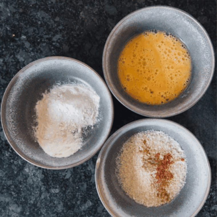 Preheating the air fryer and setting up three bowls with flour, egg, and seasoned panko breadcrumbs.