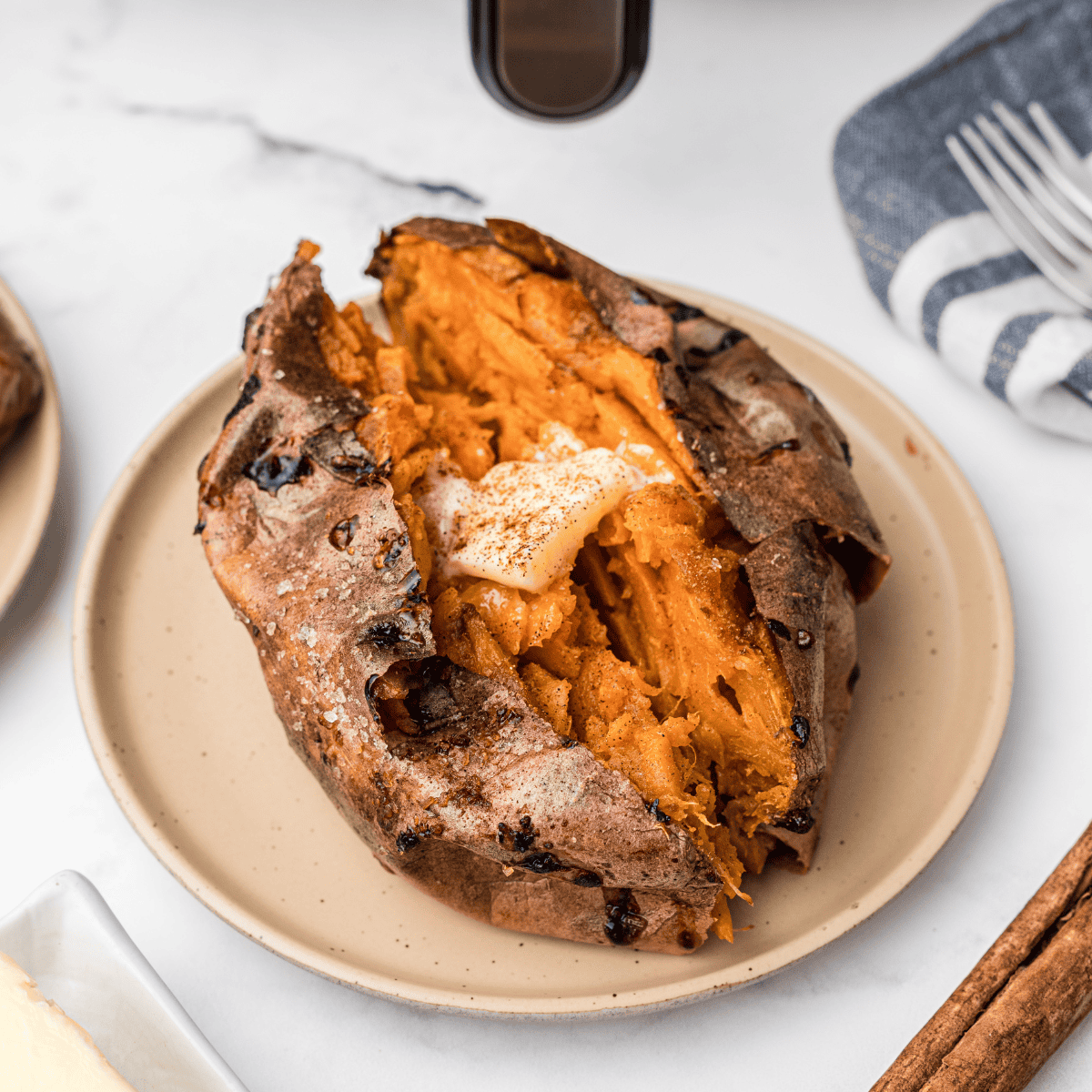 Reheated sweet potato split open in an air fryer basket, steam rising from the fluffy center with crisp skin