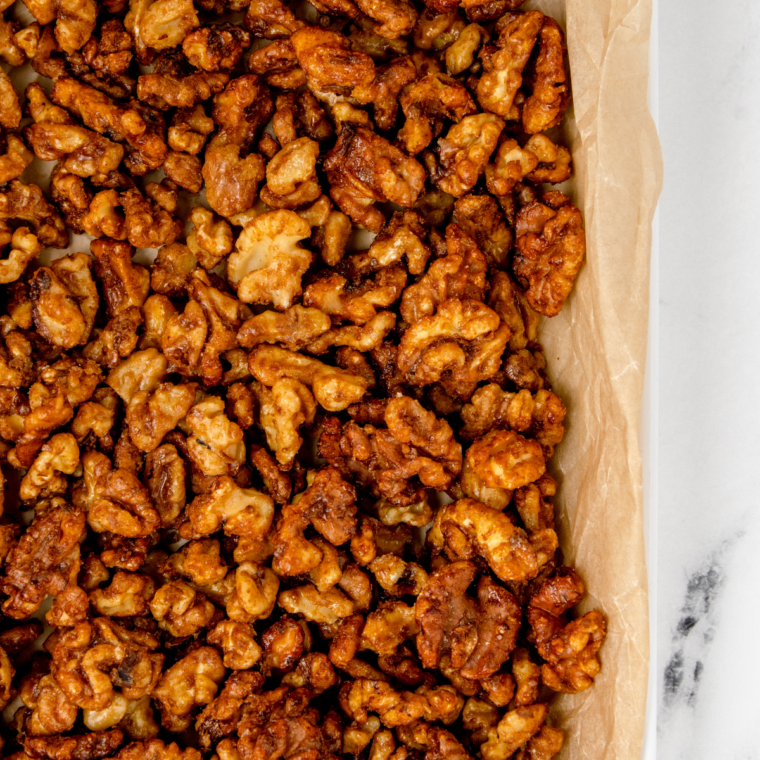 Finished honey roasted walnuts cooling on parchment paper, sprinkled with flaky sea salt, becoming crisp as they set.