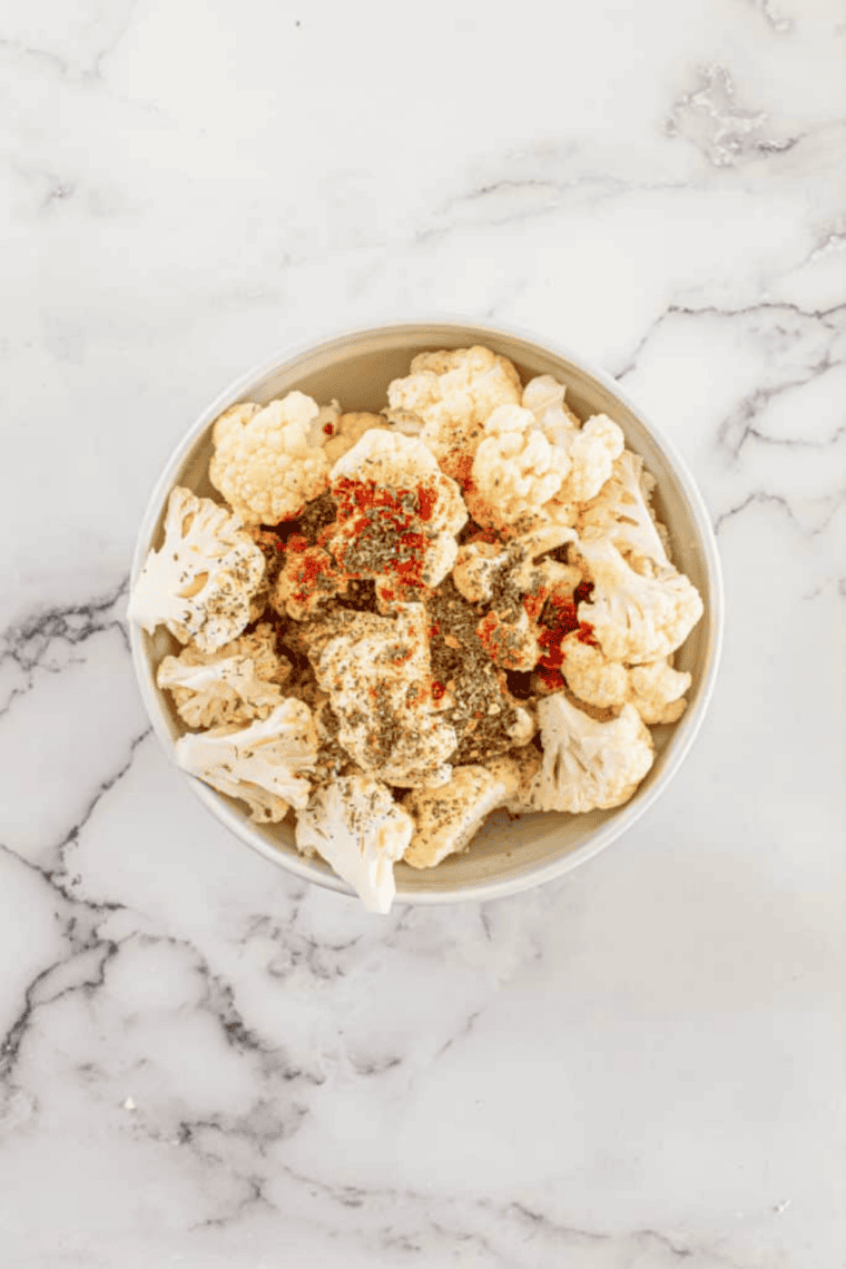 Fresh cauliflower head trimmed and cut into bite-sized florets on a cutting board.