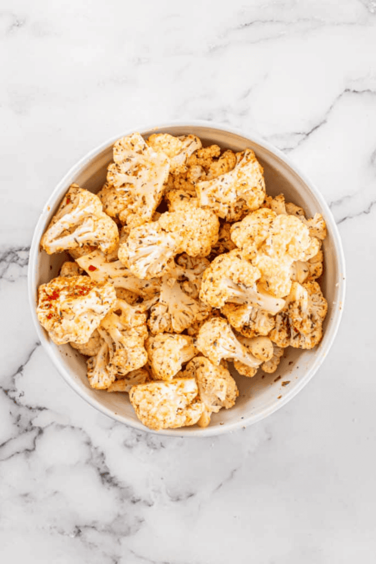 Cauliflower florets tossed with oil and spices in a large bowl, ready for air frying.