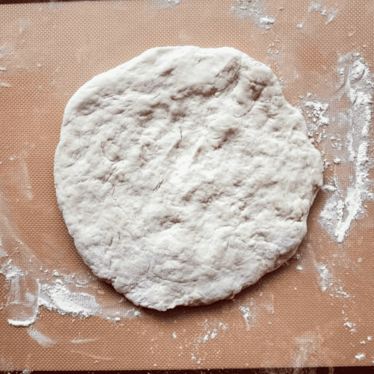 Hands pressing pizza dough into an oiled cake pan with fingertips, dough not yet reaching the edges