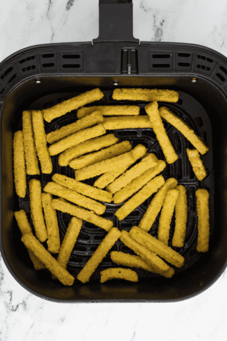 Frozen zucchini fries arranged in air fryer basket ready to cook.