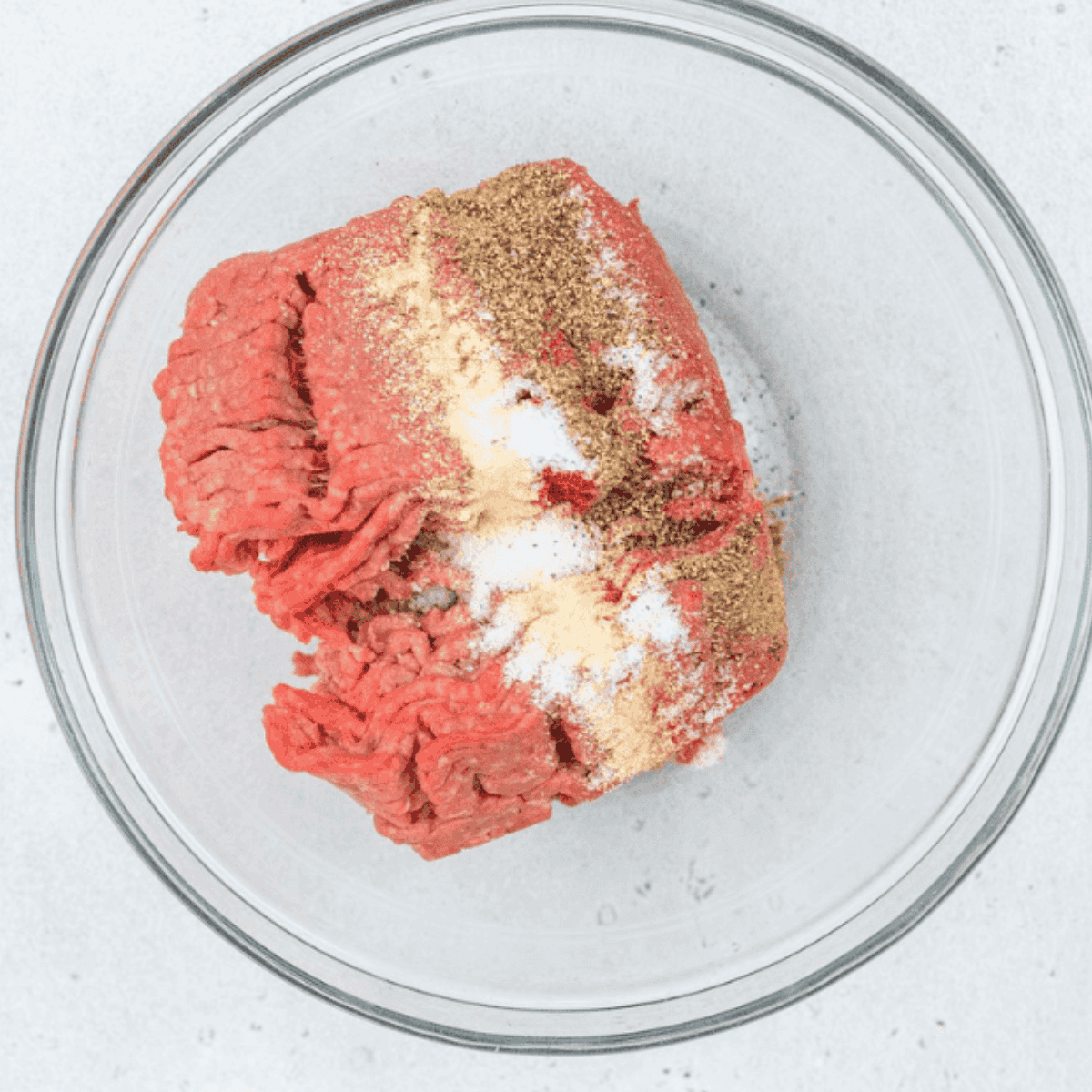 Seasoned ground beef mixed in a large bowl with garlic, onion, paprika, salt, and pepper.